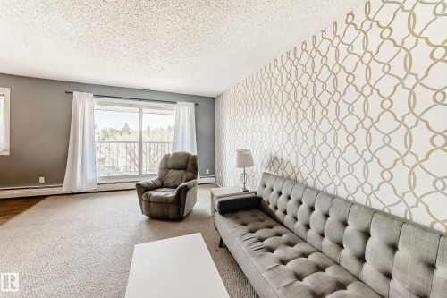 Living area featuring a patterned accent wall and large sliding glass doors opening to a balcony - 423 5125 Riverbend Road, Edmonton, AB - Indoor