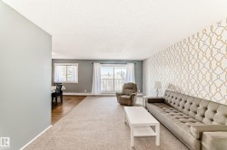 Spacious living area featuring patterned accent wall, light neutral carpeting, and a large window - 
