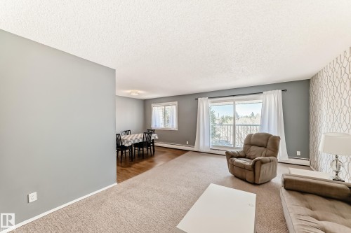 Living area featuring carpeted flooring, a patterned accent wall, and a sliding glass door opening to an outdoor space - 423 5125 Riverbend Road, Edmonton, AB - Indoor Photo Showing Living Room