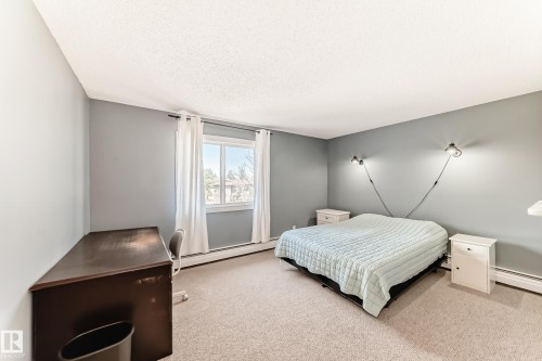 Bedroom featuring a window with white drapes, light gray walls, and light-colored carpeting - 423 5125 Riverbend Road, Edmonton, AB - Indoor Photo Showing Bedroom