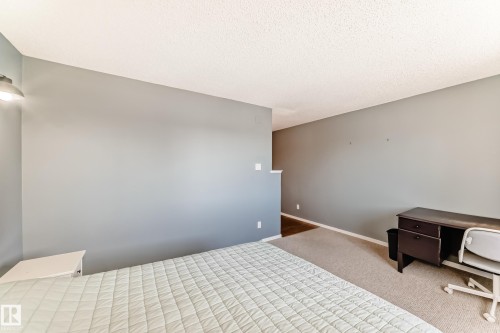 Carpeted room with light gray walls, textured ceiling, and a wall-mounted light fixture - 423 5125 Riverbend Road, Edmonton, AB - Indoor Photo Showing Bedroom