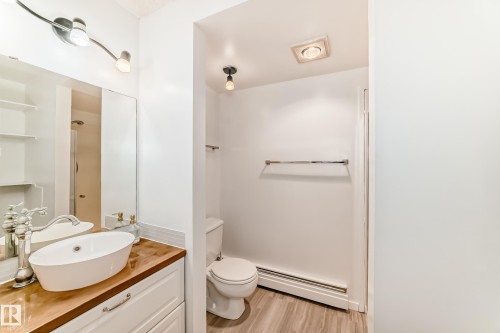 Bathroom featuring a white vessel sink on a wood-finish countertop, white vanity cabinetry with chrome hardware, and wood-finish flooring - 423 5125 Riverbend Road, Edmonton, AB - Indoor Photo Showing Bathroom