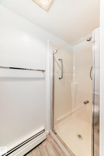 Shower enclosure featuring clear glass panels and a chrome handle, complemented by wood-finish flooring and a chrome towel bar - 423 5125 Riverbend Road, Edmonton, AB - Indoor Photo Showing Bathroom