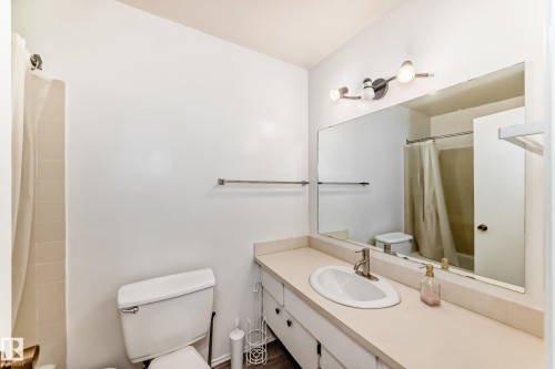 Full bathroom featuring a single vanity with an integrated sink, a large wall-mounted mirror, overhead track lighting, and a shower-tub combination with tile surround - 423 5125 Riverbend Road, Edmonton, AB - Indoor Photo Showing Bathroom