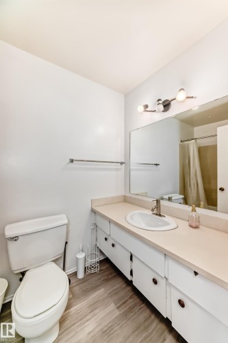 Bathroom featuring a single vanity with an integrated sink, a large wall-mounted mirror, and wood-finish flooring - 423 5125 Riverbend Road, Edmonton, AB - Indoor Photo Showing Bathroom