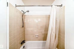 Bathtub with beige square wall tiles and a chrome shower fixture - 