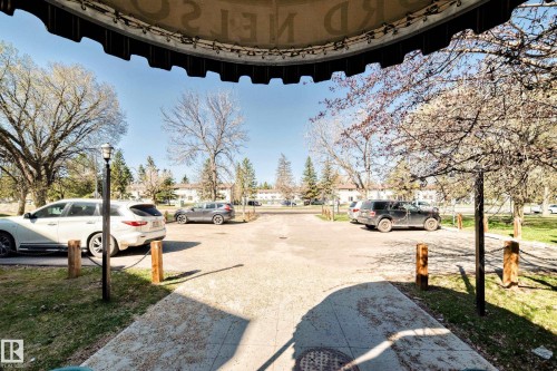 Paved parking area surrounded by mature trees and grass, featuring decorative wooden posts with chain accents and a visible street lamp - 423 5125 Riverbend Road, Edmonton, AB - Outdoor