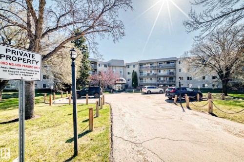 Multi-story building featuring individual balconies, a covered main entrance, and an asphalt parking area with chain-post barriers - 423 5125 Riverbend Road, Edmonton, AB - Outdoor