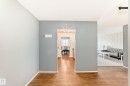 Hardwood-style flooring extends through the entryway, leading to a dining area with natural light and a separate living room featuring a patterned accent wall - 423 5125 Riverbend Road, Edmonton, AB  - Indoor Photo Showing Other Room 