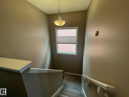 Carpeted stairway featuring a window with blinds, a modern ceiling light fixture, and a white handrail - 871 Ebbers Crescent, Edmonton, AB - Indoor Photo Showing Other Room