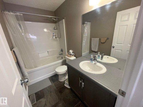 Bathroom featuring a white tub/shower combination, dark tile flooring, a dual-sink vanity with a grey countertop, a large wall-mounted mirror, and a white paneled door - 871 Ebbers Crescent, Edmonton, AB - Indoor Photo Showing Bathroom