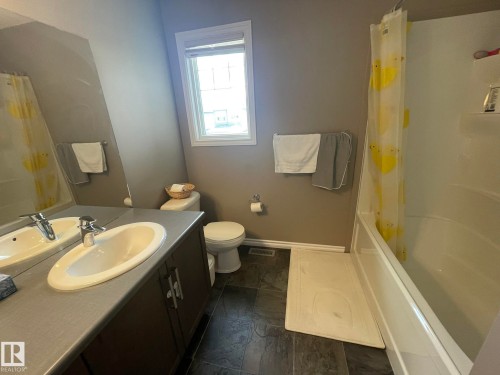 Bathroom featuring a double vanity with integrated sinks, a tub/shower combination, a white toilet, and dark stone-finish flooring - 871 Ebbers Crescent, Edmonton, AB - Indoor Photo Showing Bathroom
