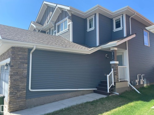 Multi-level exterior featuring dark blue siding, stone veneer accents, white trim, and a prominent front porch with steps and railing - 871 Ebbers Crescent, Edmonton, AB - Outdoor