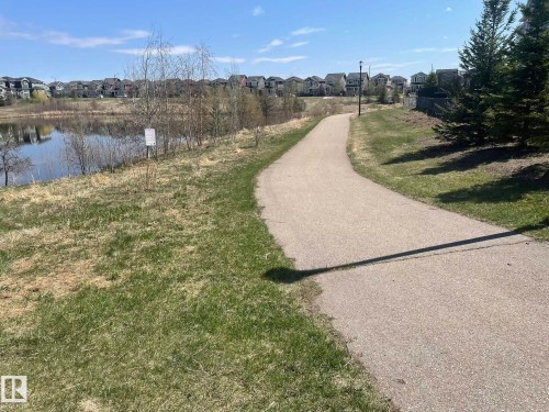 Paved pathway bordered by green grass and a body of water with residential properties in the background - 871 Ebbers Crescent, Edmonton, AB - Outdoor With View