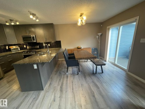 Modern kitchen featuring dark grey cabinetry, granite-style countertops, a dark subway tile backsplash, and stainless steel appliances - 871 Ebbers Crescent, Edmonton, AB - Indoor