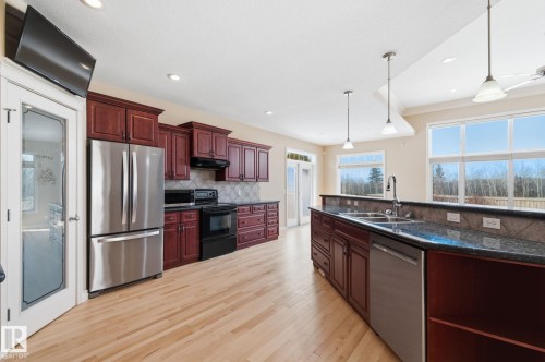 Open-concept kitchen featuring wood-finish flooring, dark wood cabinetry, stainless steel appliances, and a kitchen island with dual sinks and pendant lighting - 30 Valleyview Ridge, Fort Saskatchewan, AB - Indoor Photo Showing Kitchen With Double Sink