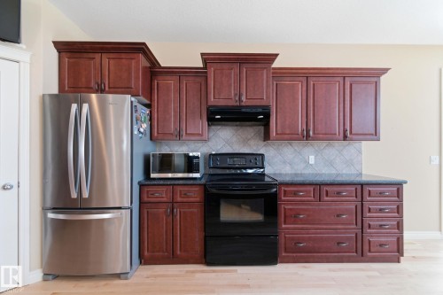 Kitchen featuring rich wood cabinetry, dark countertops, a tiled backsplash, and light wood-finish flooring - 30 Valleyview Ridge, Fort Saskatchewan, AB - Indoor Photo Showing Kitchen