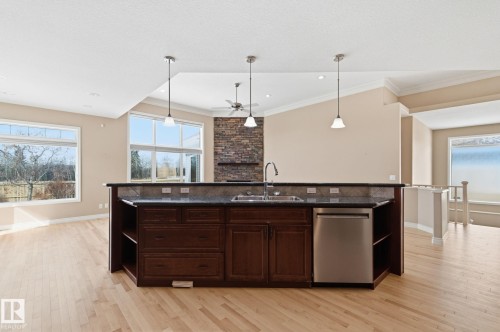 Kitchen island with a dark stone countertop, undermount sink, stainless steel dishwasher, and dark wood cabinetry - 30 Valleyview Ridge, Fort Saskatchewan, AB - Indoor Photo Showing Kitchen With Double Sink