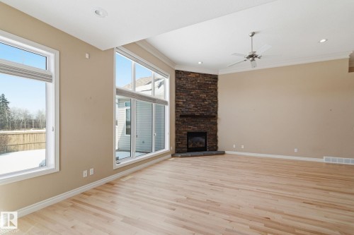 Expansive room featuring light wood-finish flooring, a corner fireplace with a stone surround and dark wood mantel, and multiple large windows - 30 Valleyview Ridge, Fort Saskatchewan, AB - Indoor With Fireplace