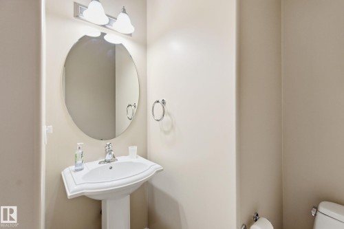 Pedestal sink with chrome faucet, oval mirror, and wall-mounted light fixture - 30 Valleyview Ridge, Fort Saskatchewan, AB - Indoor Photo Showing Bathroom