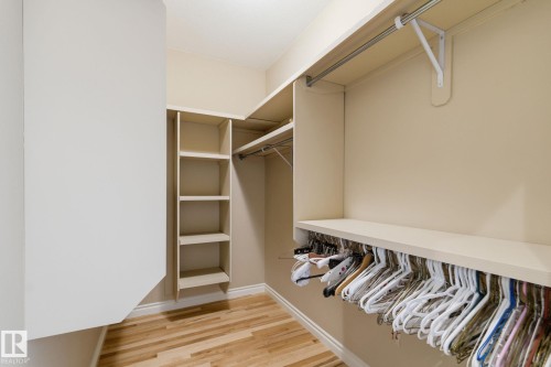 Walk-in closet featuring wood-finish flooring, built-in shelving, and multiple hanging rods for organization - 30 Valleyview Ridge, Fort Saskatchewan, AB - Indoor With Storage