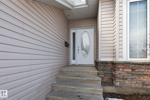 Entryway featuring a white door with an oval-shaped decorative glass insert, a stone façade, tan horizontal siding, and concrete steps - 30 Valleyview Ridge, Fort Saskatchewan, AB - Outdoor With Exterior