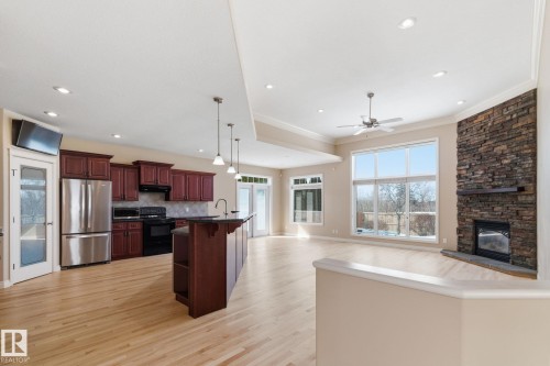 Open-concept living space featuring wood-finish flooring, a kitchen with stainless steel appliances and dark wood cabinetry, a stone-clad fireplace, and large windows - 30 Valleyview Ridge, Fort Saskatchewan, AB - Indoor Photo Showing Kitchen With Upgraded Kitchen