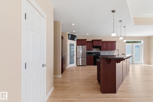 Open-concept kitchen featuring dark wood cabinetry, stainless steel appliances, and a central island with a breakfast bar - 30 Valleyview Ridge, Fort Saskatchewan, AB - Indoor Photo Showing Kitchen