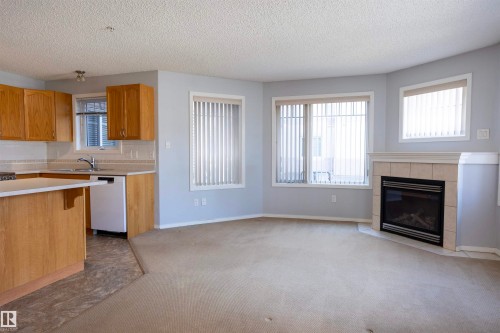 Open-concept living space featuring a corner fireplace with a tiled surround and mantel - 101 2420 108 Street, Edmonton, AB - Indoor With Fireplace