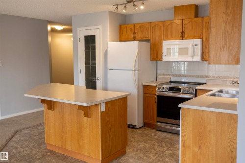 Kitchen featuring wood-finish cabinetry, track lighting, stainless steel range, and a breakfast bar island - 101 2420 108 Street, Edmonton, AB - Indoor Photo Showing Kitchen With Double Sink