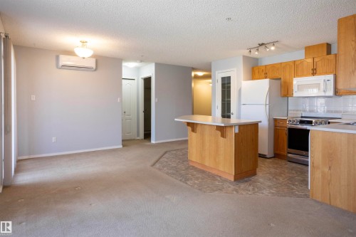Open-concept living area featuring a kitchen with wood cabinetry, white appliances, and a central island with a breakfast bar - 101 2420 108 Street, Edmonton, AB - Indoor Photo Showing Kitchen