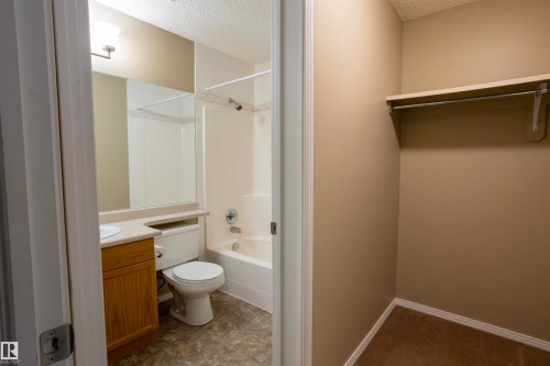 Bathroom featuring a wood-finish vanity with an integrated sink, a combination shower and tub, and a large wall-mounted mirror - 101 2420 108 Street, Edmonton, AB - Indoor Photo Showing Bathroom