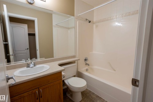 Bathroom featuring a single vanity with wood cabinetry, an integrated sink, and a large wall-mounted mirror - 101 2420 108 Street, Edmonton, AB - Indoor Photo Showing Bathroom