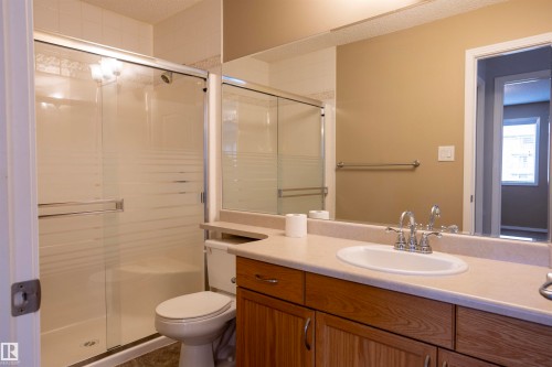 Bathroom featuring a wood-finish vanity with an integrated sink, a large mirror, and a shower enclosure with frosted glass - 101 2420 108 Street, Edmonton, AB - Indoor Photo Showing Bathroom