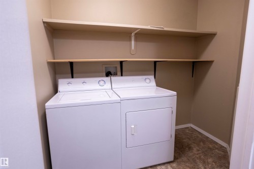 Dedicated laundry area featuring a washer and dryer, two integrated shelving units, and resilient flooring - 101 2420 108 Street, Edmonton, AB - Indoor Photo Showing Laundry Room