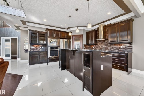 Gourmet kitchen featuring dark wood cabinetry, stainless steel appliances, a mosaic tile backsplash, a center island with pendant lighting, and white tile flooring - 1254 Adamson Drive, Edmonton, AB - Indoor Photo Showing Kitchen With Stainless Steel Kitchen With Upgraded Kitchen