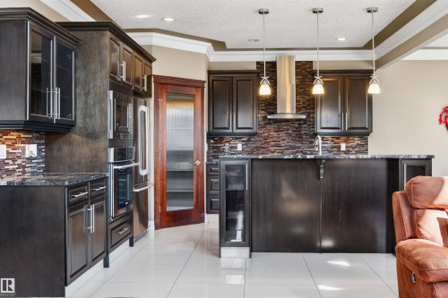 Modern kitchen featuring dark wood cabinetry, stainless steel appliances, a tiled backsplash, and recessed and pendant lighting - 1254 Adamson Drive, Edmonton, AB - Indoor Photo Showing Kitchen With Upgraded Kitchen