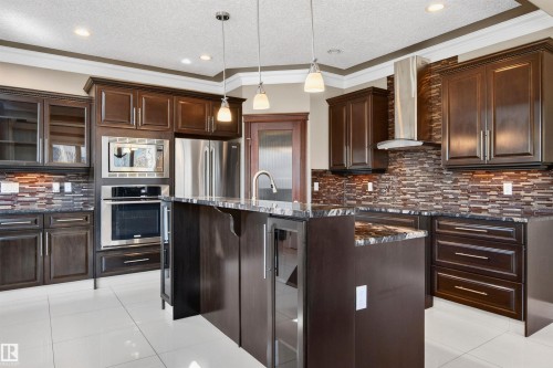 Gourmet kitchen featuring dark wood cabinetry, white tile flooring, stainless steel appliances, and a central island with a sink and pendant lighting - 1254 Adamson Drive, Edmonton, AB - Indoor Photo Showing Kitchen With Stainless Steel Kitchen With Upgraded Kitchen