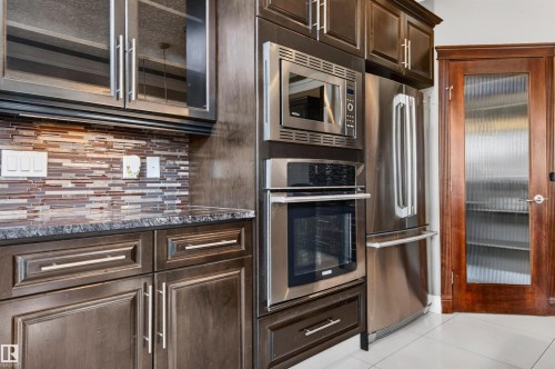 Kitchen featuring dark wood-finish cabinetry, stainless steel appliances, a mosaic tile backsplash, and a patterned countertop - 1254 Adamson Drive, Edmonton, AB - Indoor Photo Showing Kitchen With Stainless Steel Kitchen