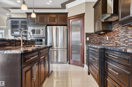 Kitchen featuring dark wood cabinetry, stainless steel appliances, patterned stone countertops, and a tiled backsplash - 1254 Adamson Drive, Edmonton, AB - Indoor Photo Showing Kitchen With Stainless Steel Kitchen With Upgraded Kitchen