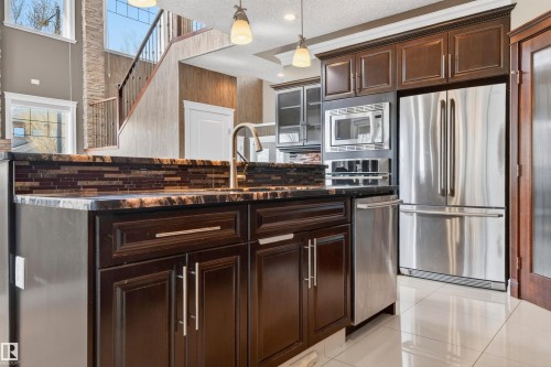 Island kitchen featuring dark wood cabinetry, a mosaic tile backsplash, and a gold-finish faucet - 1254 Adamson Drive, Edmonton, AB - Indoor Photo Showing Kitchen With Stainless Steel Kitchen