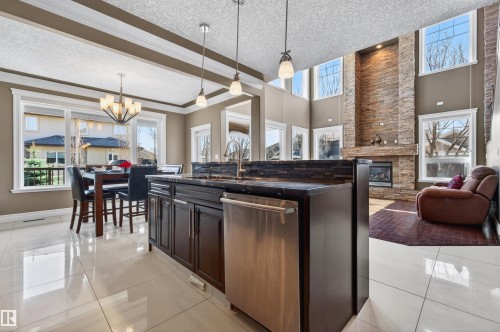 Kitchen island with dark cabinetry, integrated stainless steel dishwasher, and a dark stone countertop featuring a tiled backsplash - 1254 Adamson Drive, Edmonton, AB - Indoor