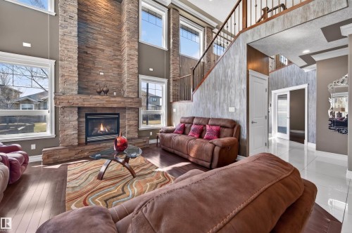Grand living area featuring a floor-to-ceiling stacked stone fireplace, dark wood-finish flooring, and multiple large windows - 1254 Adamson Drive, Edmonton, AB - Indoor Photo Showing Living Room With Fireplace