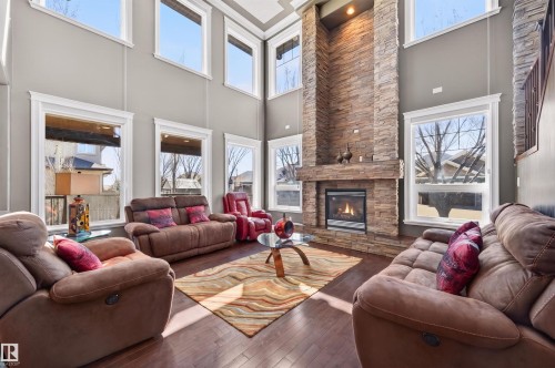 Two-story living room featuring a floor-to-ceiling stone-clad fireplace, dark wood-finish flooring, and multiple large windows with white trim - 1254 Adamson Drive, Edmonton, AB - Indoor Photo Showing Living Room With Fireplace