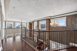 Upper-level landing featuring dark wood-finish flooring, wrought iron railings, multiple windows, recessed lighting, and a contemporary chandelier - 
