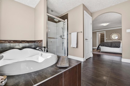 Bathroom featuring a built-in jetted tub with tile surround, glass-enclosed shower, dark large-format floor tiles, and a wide arched doorway - 1254 Adamson Drive, Edmonton, AB - Indoor Photo Showing Other Room