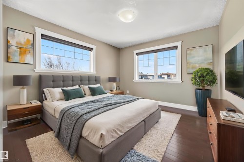 Spacious sleeping area featuring dark wood-finish flooring, two large multi-pane windows with white trim, light neutral wall paint, and a white ceiling light fixture - 1254 Adamson Drive, Edmonton, AB - Indoor Photo Showing Bedroom