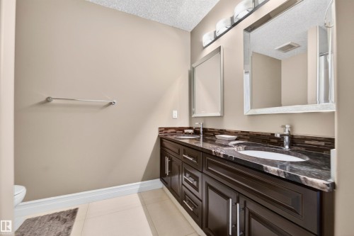 Dual sink vanity featuring dark wood cabinetry, a dark stone countertop, and two undermount sinks - 1254 Adamson Drive, Edmonton, AB - Indoor Photo Showing Bathroom