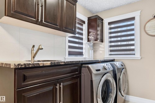 Dedicated utility area featuring dark wood-finish cabinetry, a large sink with a brushed metal faucet, a dark stone-finish countertop, and white square tile backsplash - 1254 Adamson Drive, Edmonton, AB - Indoor Photo Showing Laundry Room