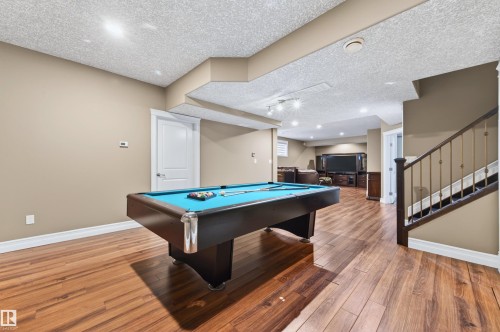 Spacious recreation room featuring wood-finish flooring, recessed lighting, and a staircase with dark wood newel posts and metal balusters - 1254 Adamson Drive, Edmonton, AB - Indoor Photo Showing Other Room